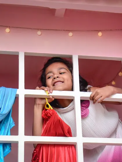 A happy girl peeks out from the window of our pink playhouse, a favorite spot for imaginative games.