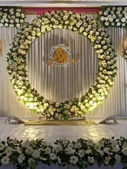 A classic engagement stage with a large circular arch made of white flowers, featuring a Ganesha emblem in the center for blessings.