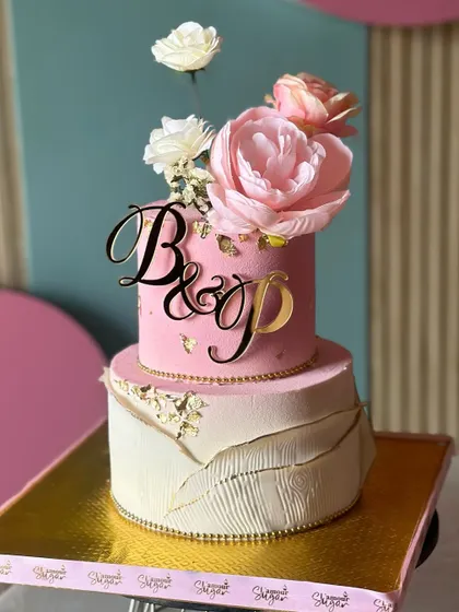 A dreamy and elegant wedding cake in shades of pink and white. This design features a textured bottom tier, a floral-topped upper tier, and a custom initial topper.