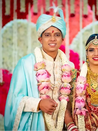 A classic wedding portrait of a couple adorned with beautiful lotus garlands, posing against a floral backdrop.