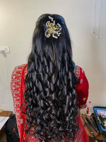 A reception hairstyle with long, defined curls and a half-updo, adorned with a sparkling gold and pearl accessory.
