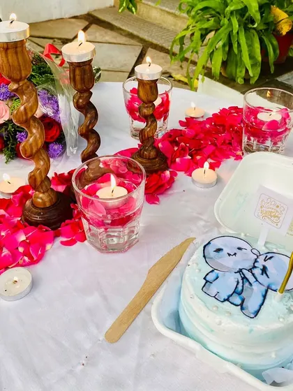 A close-up of a romantic table setting for two. The decor includes floating candles, rose petals, and a cute custom bento cake.