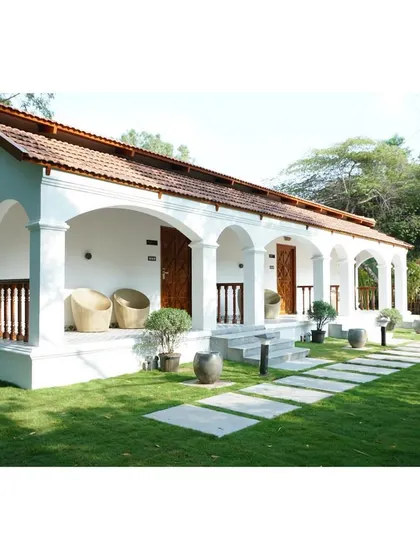A daytime perspective of the villa, showing how the white walls and terracotta roof stand out against the green landscape. The open verandas provide shaded seating areas for residents to enjoy the outdoors.