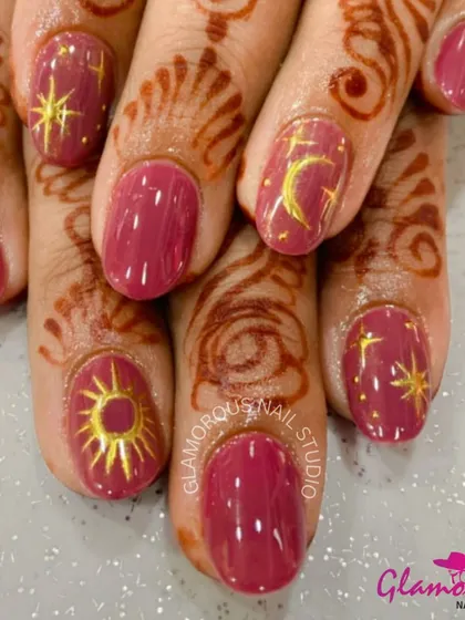 Celestial-themed nails for a festive celebration. This design features a rich mauve base adorned with hand-painted golden sun, moon, and star motifs that beautifully complement the henna.