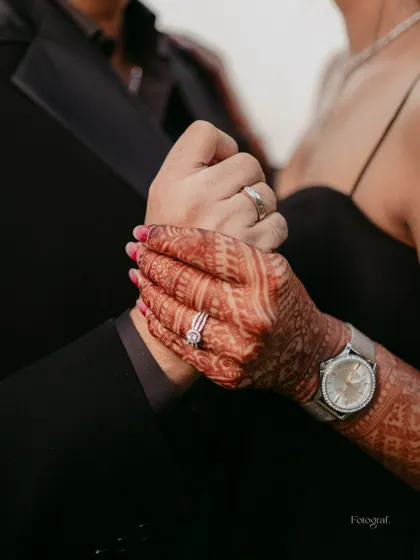 A close-up detail shot of the couple holding hands, showing their rings and the bride's intricate henna design.