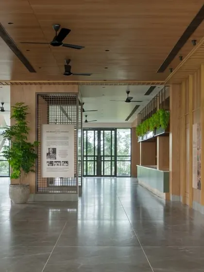 A wider view of the spacious auditorium lobby. This multi-functional pre-event area includes casual seating, a refreshment counter, and informational displays, all designed with a warm and natural material palette.