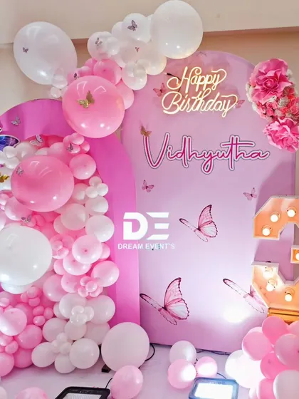 A beautiful pink butterfly-themed setup for a third birthday, complete with a custom name sign, a 'Happy Birthday' neon light, and a large marquee number '3'.