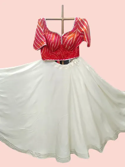 The pure white skirt of this lehenga creates a beautiful contrast with the vibrant red bandhani-style blouse, shown here in full flare.