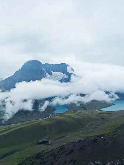 The turquoise water of Gadsar Lake is partially visible through a break in the clouds, with a mountain peak rising above. This is a typical, breathtaking view on the KGL trek.