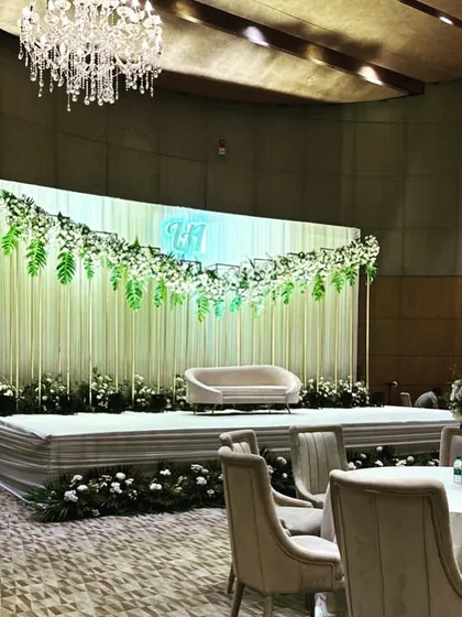 A sophisticated stage for a Roka ceremony, featuring a backdrop of white drapes, hanging greenery, and a custom neon monogram for the couple.