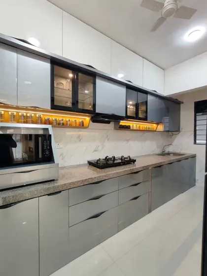 A sleek, straight-line kitchen with glossy grey cabinets and a granite countertop. The open spice rack with warm backlighting is a practical and beautiful feature, keeping essentials within easy reach.