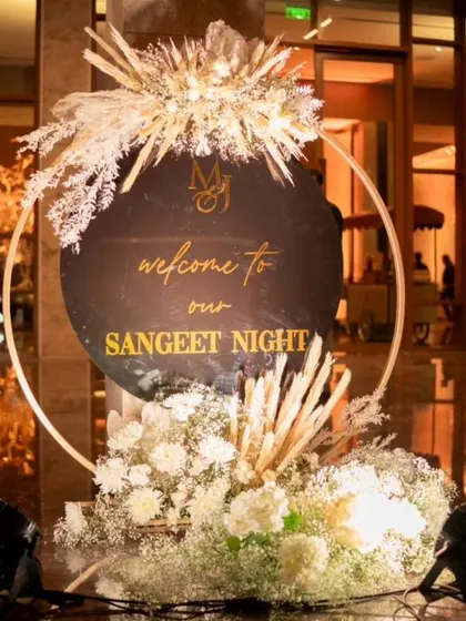 A stylish welcome sign for the Sangeet, featuring a black and gold design with dried floral accents.