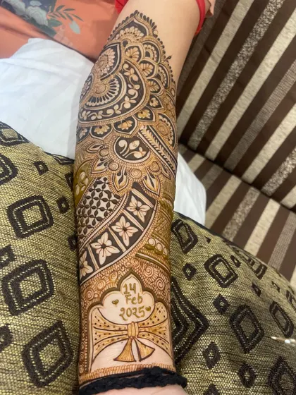 A beautiful design featuring the wedding date, "14 FEB 2025", placed within a heart inside a traditional 'shehnai' or turban motif on the arm.