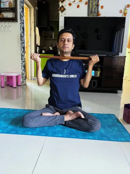 A client demonstrates a seated posture using a stick to open the shoulders and chest, a simple yet effective technique for improving posture.