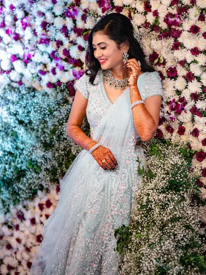 For a modern reception or sangeet, we can create something truly magical. I loved styling this shimmering lehenga with soft, romantic curls and a makeup look that felt glamorous yet effortless against this beautiful flower wall.
