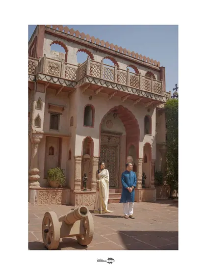 A wide shot establishing the grandeur of the heritage location. The couple stands in traditional attire, creating a portrait that feels like a painting from a bygone era.
