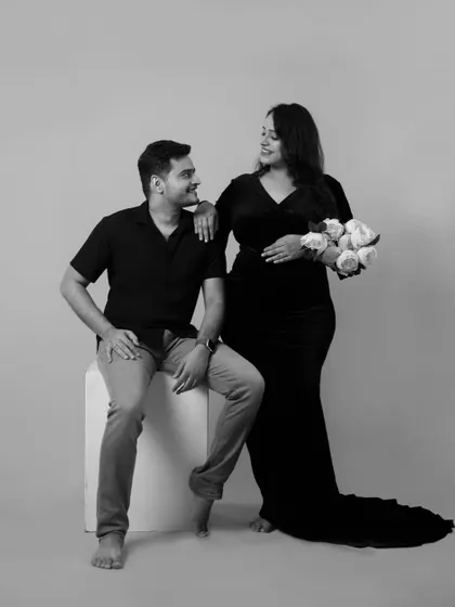 A classic couple's pose in our studio. The mother-to-be holds a bouquet of white roses, adding a touch of elegance to this black and white maternity portrait.