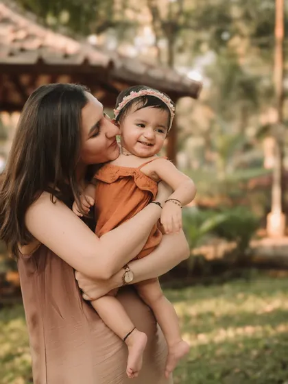 A mother shares a sweet, affectionate moment with her daughter against a beautiful, soft-focus park background.