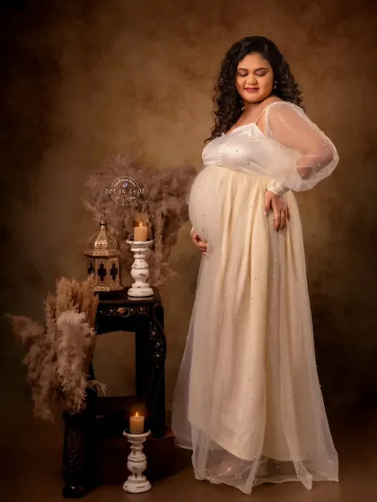 A glowing mom-to-be in a cream-colored gown, surrounded by the warm ambiance of candles and rustic decor.
