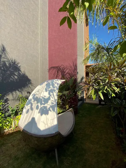 A cozy, private court designed as a green oasis. The unique boat-like outdoor furniture provides a comfortable spot for relaxation, surrounded by lush tropical plants that create a sense of enclosure and escape.