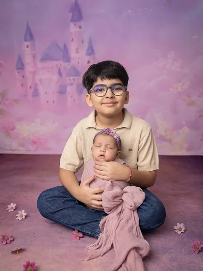 A brother's protective embrace. He sits with his new baby sister, a quiet guardian in a whimsical, castle-themed setting.