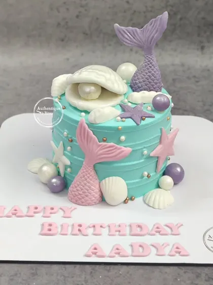 A beautiful mermaid cake with pink and purple mermaid tails, seashells, and pearls.