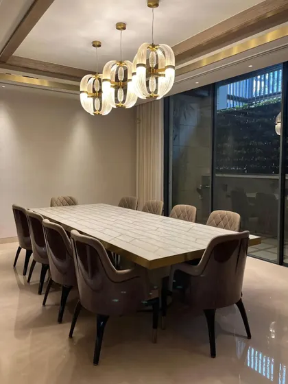 A closer view of the dining set, highlighting the contrast between the textured, patterned tabletop and the smooth, velvety upholstery of the chairs. The warm light from the pendant fixtures enhances the rich materials and inviting atmosphere.