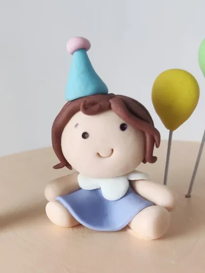 A close-up of the adorable fondant girl topper, complete with a tiny party hat. It's the perfect finishing touch for a first birthday cake.