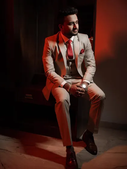 A groom sits for a portrait, bathed in dramatic red lighting that highlights his stylish reception suit. We use creative lighting to produce bold and modern groom portraits.