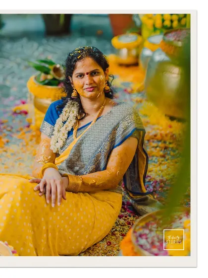 The bride, covered in turmeric paste, smiles for the camera in a moment of calm during her vibrant Haldi ceremony.