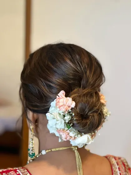 This intricate wedding bun is decorated with a mix of peach and white flowers, creating a soft and elegant look. It’s a perfect hairstyle for a bride wearing a traditional red lehenga.