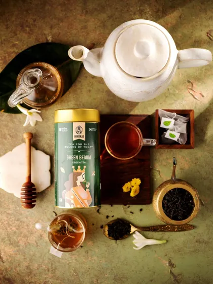 A beautiful flat lay of Hindraj's Green Begum tea. The composition includes a teapot, loose tea leaves, and a honey dipper, creating a complete and aesthetically pleasing story about the ritual of tea.