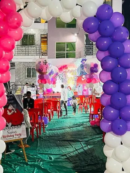 A vibrant balloon arch entrance for an outdoor birthday party. The pink, purple, and white colors welcome guests into the celebration area.