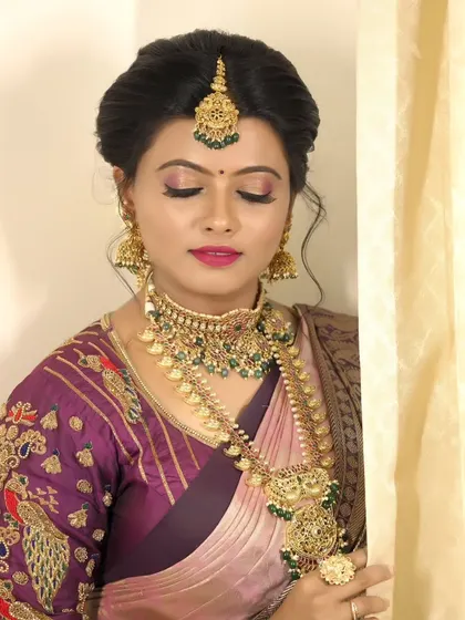 A beautiful bridal makeup look, featuring a model in a traditional purple silk saree with an embroidered blouse and heavy gold jewelry.