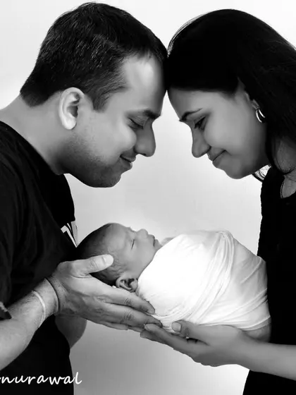 A timeless black and white photo of new parents holding their sleeping baby together, their faces close in a tender moment that speaks of love and new beginnings.