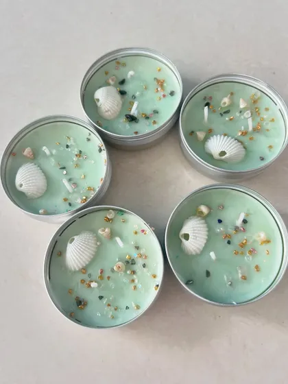 A set of five beach-themed travel tin candles, with tiny shells and crystals.