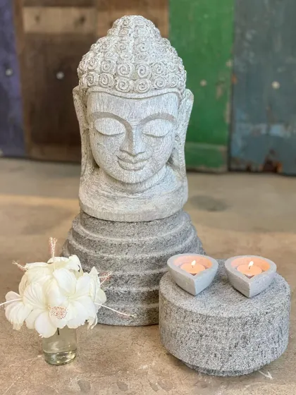 A serene Buddha bust carved from stone, paired with simple candle holders, creates a peaceful vignette for meditation or decor.