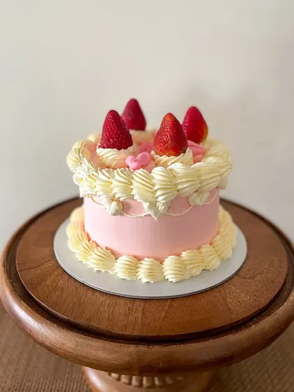 A sweet and simple vintage-style cake. This pink buttercream cake is decorated with classic piping, topped with fresh strawberries for a fresh and pretty look.