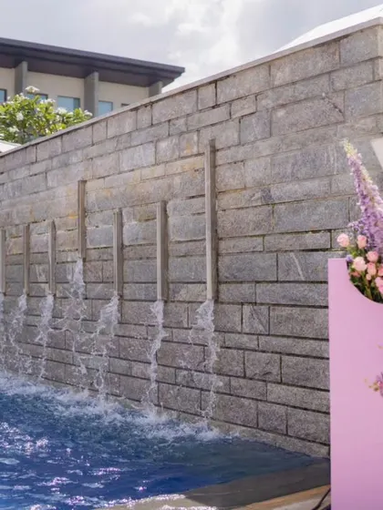 A custom prop with purple flowers stands next to a waterfall feature at the poolside venue.