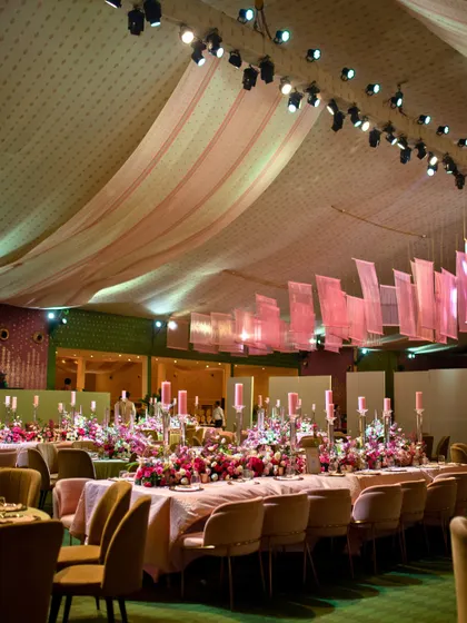 The reception dinner for a Delhi wedding, featuring long tables adorned with lush pink florals and tall candles. The soft lighting and elegant setup created a warm and inviting ambiance for families to celebrate together.