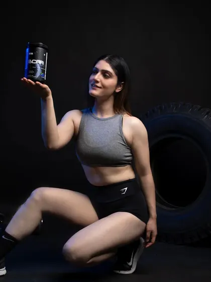 A female model in a dynamic pose, presenting a BCAA supplement container. The lighting and pose are designed to be eye-catching and energetic.