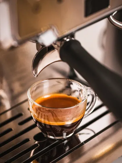 A finished shot of espresso in a glass cup, sitting on the machine's drip tray. This clean, final-product shot is perfect for menus or websites.