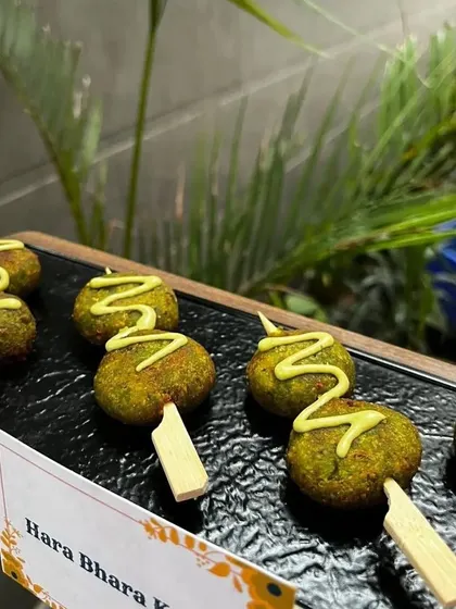 A popular vegetarian appetizer, Hara Bhara Kebab. These spinach and pea patties are served on sticks with a drizzle of sauce, making them a perfect bite-sized snack.