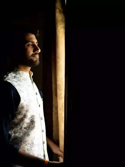 A thoughtful portrait of the groom looking out a window. The natural light creates a cinematic mood, capturing a moment of quiet reflection on his wedding day.