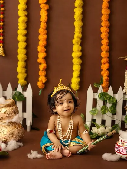 A solo shot of a baby boy dressed as Krishna, sitting in a charmingly decorated festive scene.