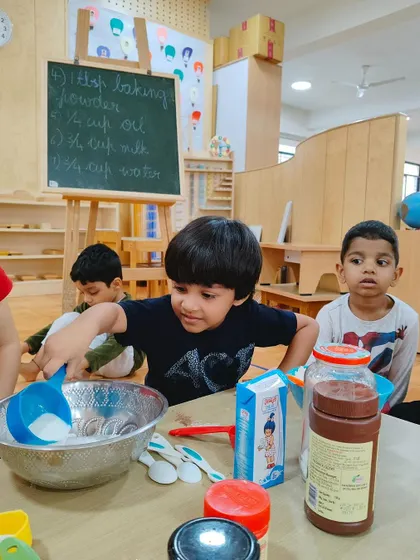 Another child takes his turn to pour ingredients into the bowl. Each step of the baking process is a valuable learning opportunity that builds confidence.