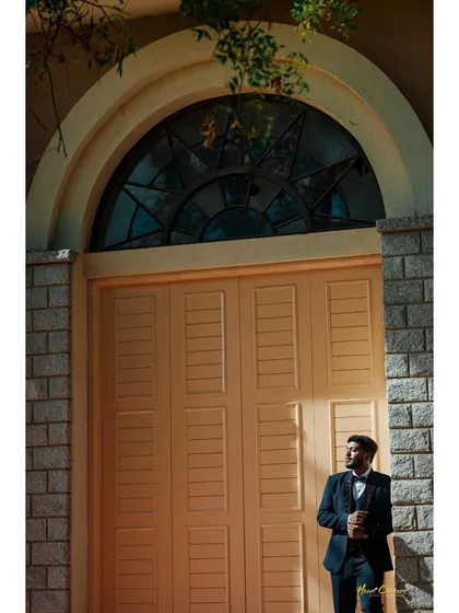 The groom looking sharp in a classic tuxedo, waiting by a grand doorway. This solo portrait captures the anticipation and style of the wedding day.