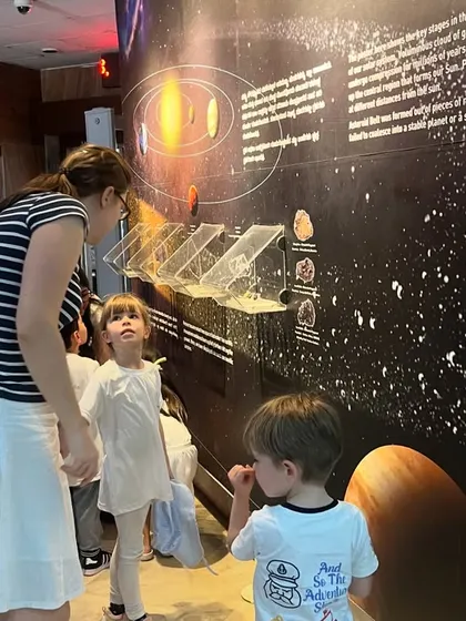 A teacher and students look up at a large display about the formation of planets, sparking their curiosity about space.