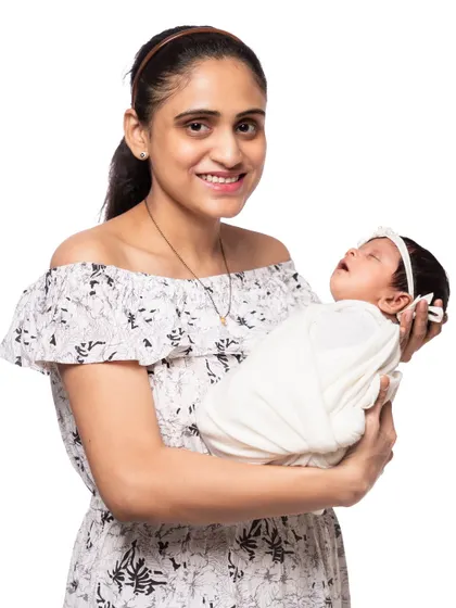 A beautiful portrait of a mother holding her sleeping baby. Her bright smile and the baby's peaceful expression make this a heartwarming image that radiates pure happiness.