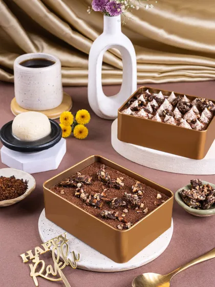 A wider shot of the Rakhi-themed Rasgulla Tiramisu, styled with coffee and flowers to create a sophisticated fusion look.